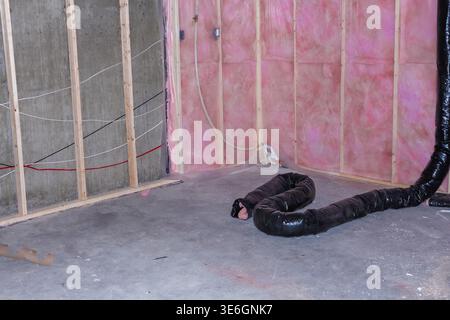 Interior view of a construction site featuring exposed wooden framing, pink insulation, and a black ventilation duct on the floor Stock Photo