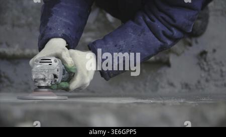 Builder worker with grinder machine cutting finishing concrete wall at construction site. Clip. Worker grinds concrete wall Stock Photo