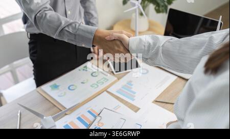 Two professionals shaking hands over ESG documents, representing a commitment to sustainable business practices Stock Photo