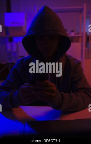 A mysterious hooded hacker working on a computer in a dark room. A concept for cybersecurity, hacking, cybercrime, and data privacy threats Stock Photo