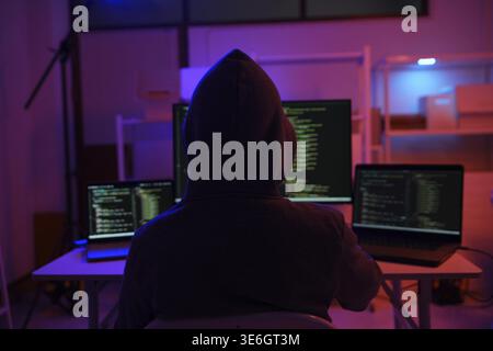 A mysterious hooded hacker working on a computer in a dark room. A concept for cybersecurity, hacking, cybercrime, and data privacy threats Stock Photo