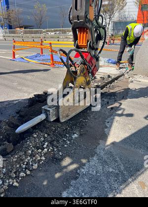 Seoul, South Korea - April 2026: Construction worker in safety vest and helmet drilling concrete on a street during road repair work Stock Photo