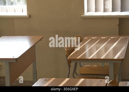 A classroom scene features empty desks and chairs bathed in natural sunlight, casting shadows and illuminating the space. Stock Photo