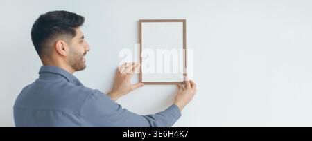 Man Holds Empty Frame on Wall While Smiling During Home Decoration Activity at Daytime Stock Photo