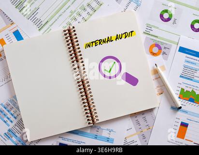 Notebook displaying internal audit with a check mark and magnifying glass icon, placed on financial documents, signifying a successful audit process Stock Photo