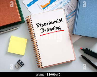 Notebook with experiential branding handwritten on it, placed on desk with pen, highlighter, documents, books, sticky notes and binder clip Stock Photo