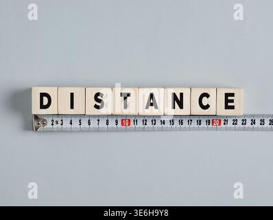 Wooden cubes composing the word distance with a measuring tape below, conveying the concept of measuring distance Stock Photo