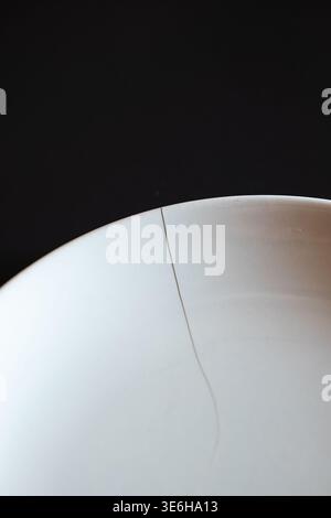 Top down, macro shot of a cracked white ceramic plate against a dark background. Natural light, no people Stock Photo