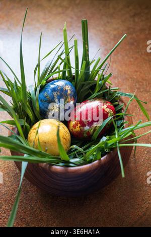Three colorful hand painted easter eggs with gold foil in a wooden bowl filled with green grass. Top down view, natural window light, no people Stock Photo