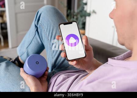 A man holds a smartphone with the Yandex Alice AI app and adjusts the Alice speaker. Saint Petersburg, Russia - 7 Apr 2026 Stock Photo
