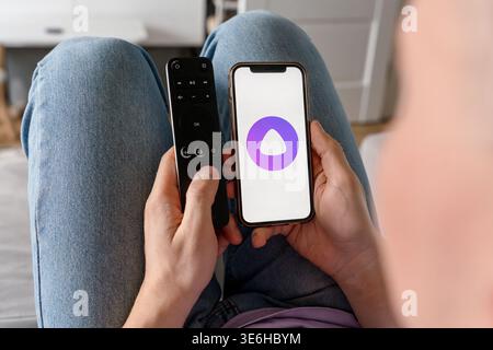 A man holds a smartphone with the Yandex Alice AI app and adjusts the TV remote. Saint Petersburg, Russia - 7 Apr 2026 Stock Photo