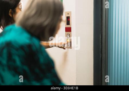 Woman pressing elevator button with senior woman in a building hallway Stock Photo