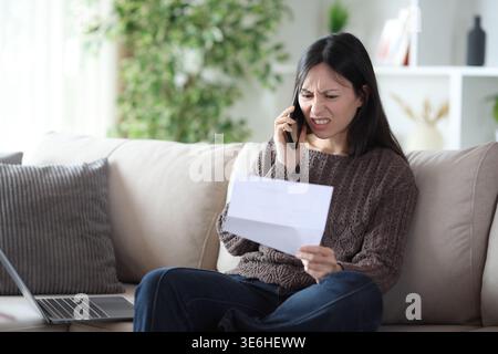 Angry asian woman claiming on phone about paper document sitting on a couch at home Stock Photo