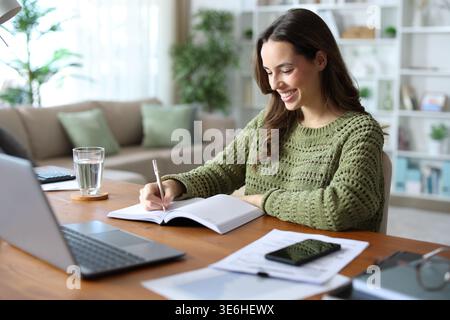 Happy employee teleworking at home writing in paper agenda Stock Photo