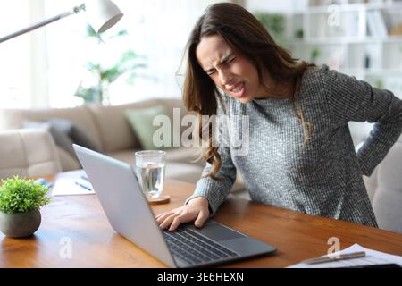Stressed tele worker suffering back ache on uncomfortable chair working at home Stock Photo
