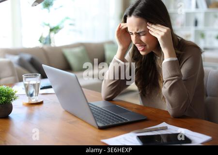 Stressed tele worker suffering migraine attack and complaining while working at home Stock Photo
