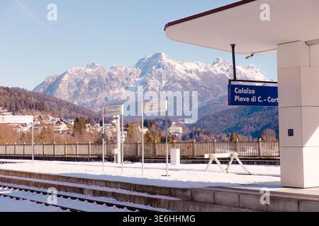 Cortina, Italy - January 27, 2026: Snowy train station platform featuring signs for Calalzo and Pieve di Cadore with majestic mountains in the backgro Stock Photo