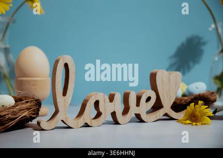 Wooden word LOVE traditional greeting to christian holiday. Festive mood composition with bunnies and yellow flowers on pastel blue background. Sustainable natural materials decorations Stock Photo