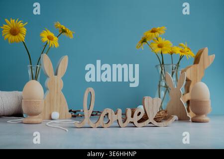 LOVE wooden word on festive blue background and eco-friendly zero waste natural decoration. Yellow daisies flowers. Bunny egg. Holiday greeting card Stock Photo