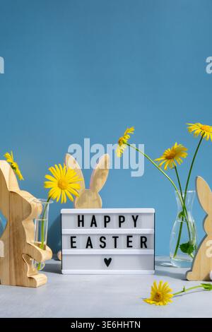 Lightbox with message HAPPY EASTER on festive blue background and eco-friendly zero waste natural decoration. Yellow daisies flowers. Holiday greeting card Stock Photo