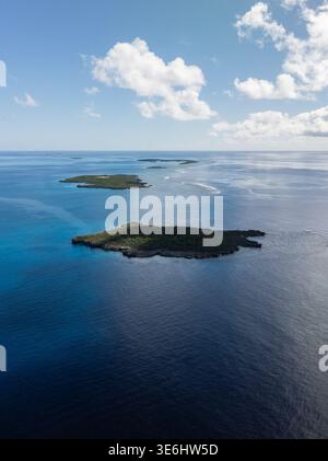 Aerial view of small islands scattered across the deep blue sea, contrasting with the bright sky and scattered clouds, Ouvéa, Loyalty Islands Province Stock Photo