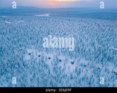 A breathtaking view of Akaslompolo in Lapland, featuring a vast expanse of snow-covered forests. The setting sun casts a warm glow, creating a magical winter atmosphere. Stock Photo