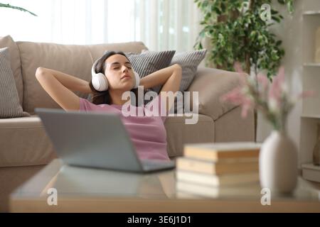 Woman wearing headphone relaxing leaning on a couch listening music beside a laptop Stock Photo
