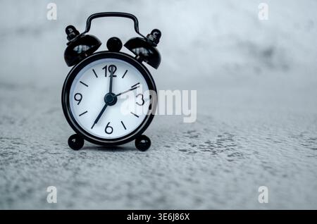 Clean black alarm clock thumbnail presenting a seven o clock morning time setting against a soft neutral surface backdrop. Stock Photo