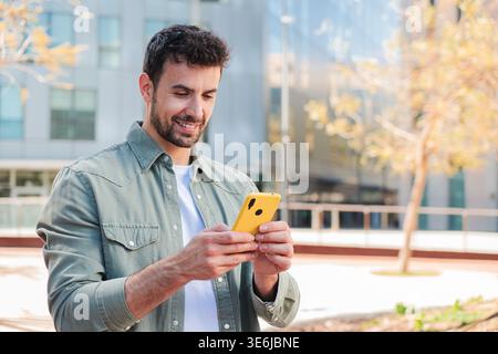 A man enjoying a focused moment while using a smartphone to connect and communicate with others in a lively outdoor space, showcasing modern Stock Photo