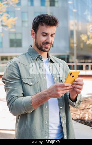 A young man interacts with his smartphone, absorbed in the screen while enjoying a sunny day outdoors. His focused expression suggests he is either Stock Photo