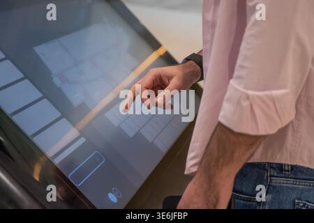 Close view of a man using a touchscreen kiosk interface in a modern indoor environment. Concept of digital technology, self service systems, and user Stock Photo