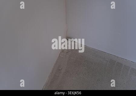Close view of a crack in the wall corner near the floor in an unfinished interior space. Concept of construction defects, structural issues, and moist Stock Photo