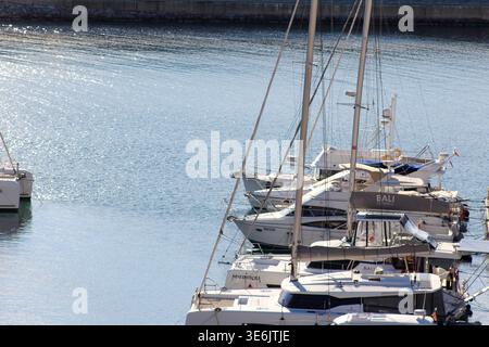 Modern yachts and catamarans moored in a calm marina with sparkling blue water on a bright sunny day. Stock Photo