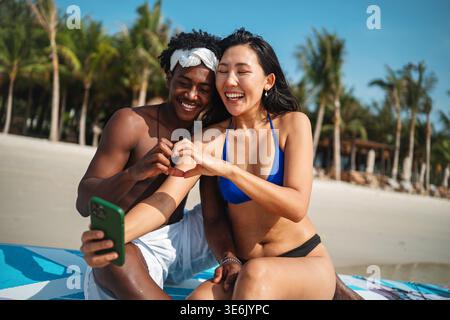 Trendy digital creator couple taking selfie by the beach, sharing travel content for social media Stock Photo