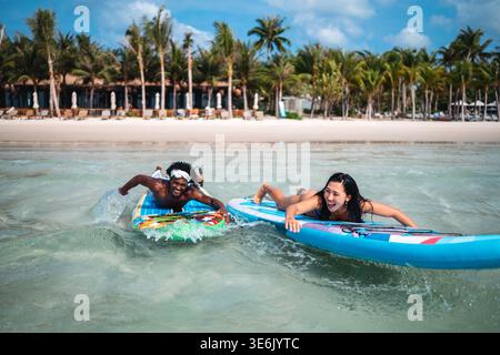 Young multiethnic people, couple having fun on surfboards in the clear ocean water during summer Stock Photo
