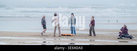 A  panoramic image of a group of people friends playing a game with a ball at low tide on Fistral Beach on the coast of Newquay in Cornwall in the UK. Stock Photo