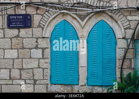 Colorful, painted, turquoise metal shutters frame a pair of arched windows on an old stone building in Jerusalem, Israel. Stock Photo