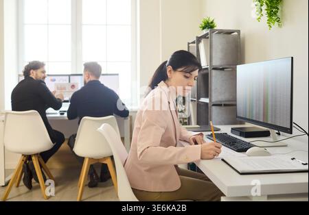 Focused woman working at computer, men collaborating in modern office workspace Stock Photo