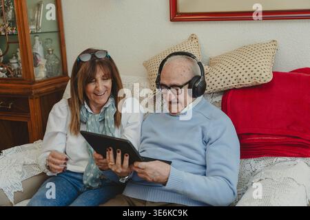 Older man wearing headphones and his daughter laughing while looking at a tablet Stock Photo