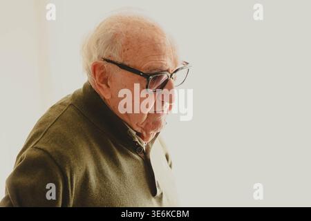 Senior man with white hair and glasses facing right in a pensive moment Stock Photo