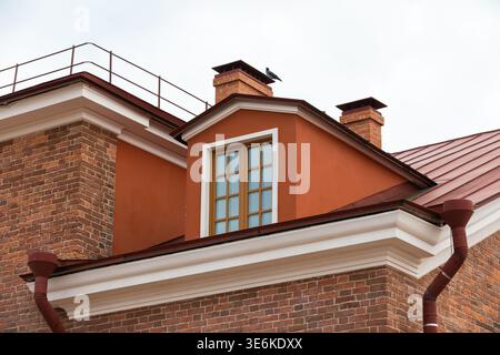 A red roof dormer with a multi-pane window and brick chimneys on a historic urban building, highlighting architectural textures, warm earth tones and Stock Photo