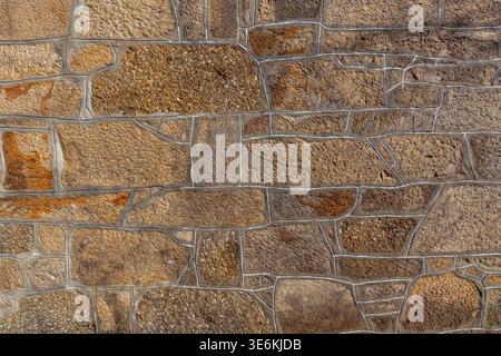 A close-up texture shot of a rustic stone wall made of rough-hewn beige and brown granite blocks with distinct white mortar joints. Stock Photo