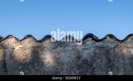 Old textured concrete wall with a wavy corrugated edge, closeup view. Blue sky background Stock Photo
