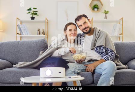Couple watching movie with home projector on sofa, eating popcorn in cozy room Stock Photo