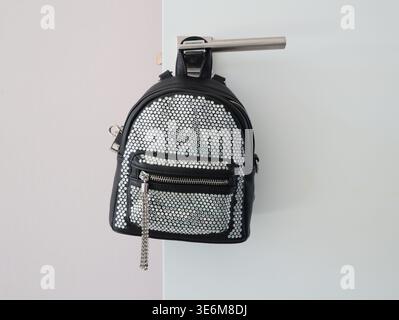 Stylish black leather bag with decorative stones hanging on a door handle in a room Stock Photo