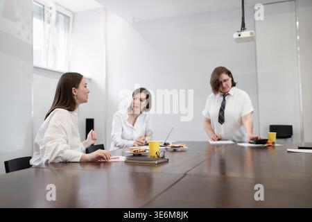 Meeting of female team members in white shirts discussing at office table with drinks and laptops. Team, drinks, laptops, meeting, discussion, white Stock Photo