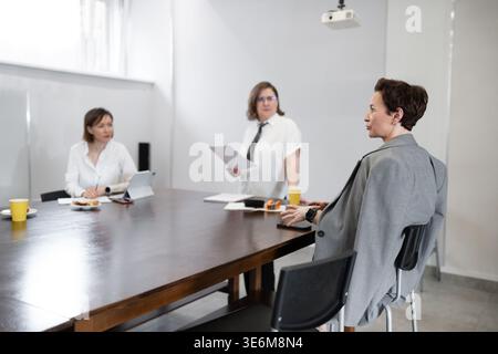 Professional women standing and talking with colleagues at wooden office table in modern workplace. Talking, standing, table, women, office Stock Photo