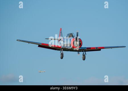 Shiny silver and red vintage trainer warbird approaches for landing at an airshow over a clear blue sky in the USA, showcasing historic military aviat Stock Photo