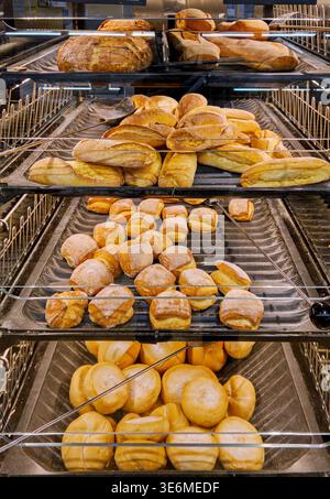 Fresh bread self-service display in supermarket featuring various types of baked goods, such as large loaves, baguettes, and buns. Stock Photo