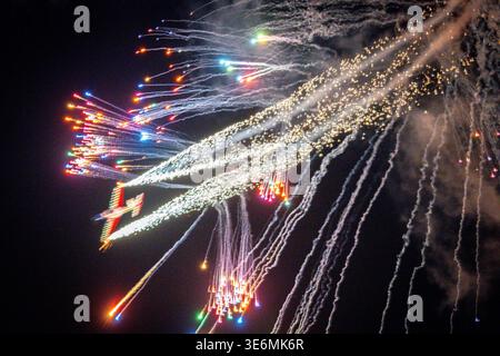 A stunt airplane cuts across a dark night sky releasing colorful fireworks and glittering sparks during an airshow, captured with long exposure to emp Stock Photo
